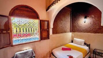 A room with a bed, a chair, a window with a view of a garden, and an arched ceiling.