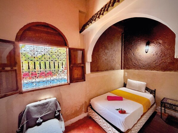 A room with a bed, a chair, a window with a view of a garden, and an arched ceiling. - Riad Belgika (Ourika)