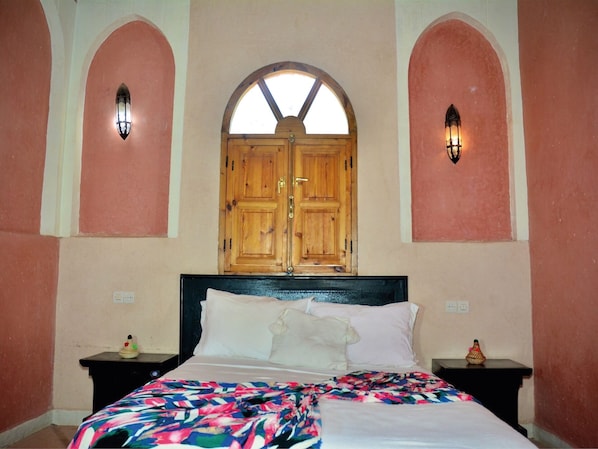 A bedroom with a large bed, two nightstands, a wooden wardrobe, and two wall-mounted lights.