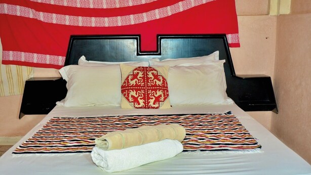 A neatly made bed with a patterned blanket, a decorative pillow, and a rolled towel.