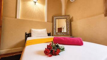 A hotel room with a bed, a wall-mounted air conditioner, a decorative mirror, and a wall-mounted light fixture.