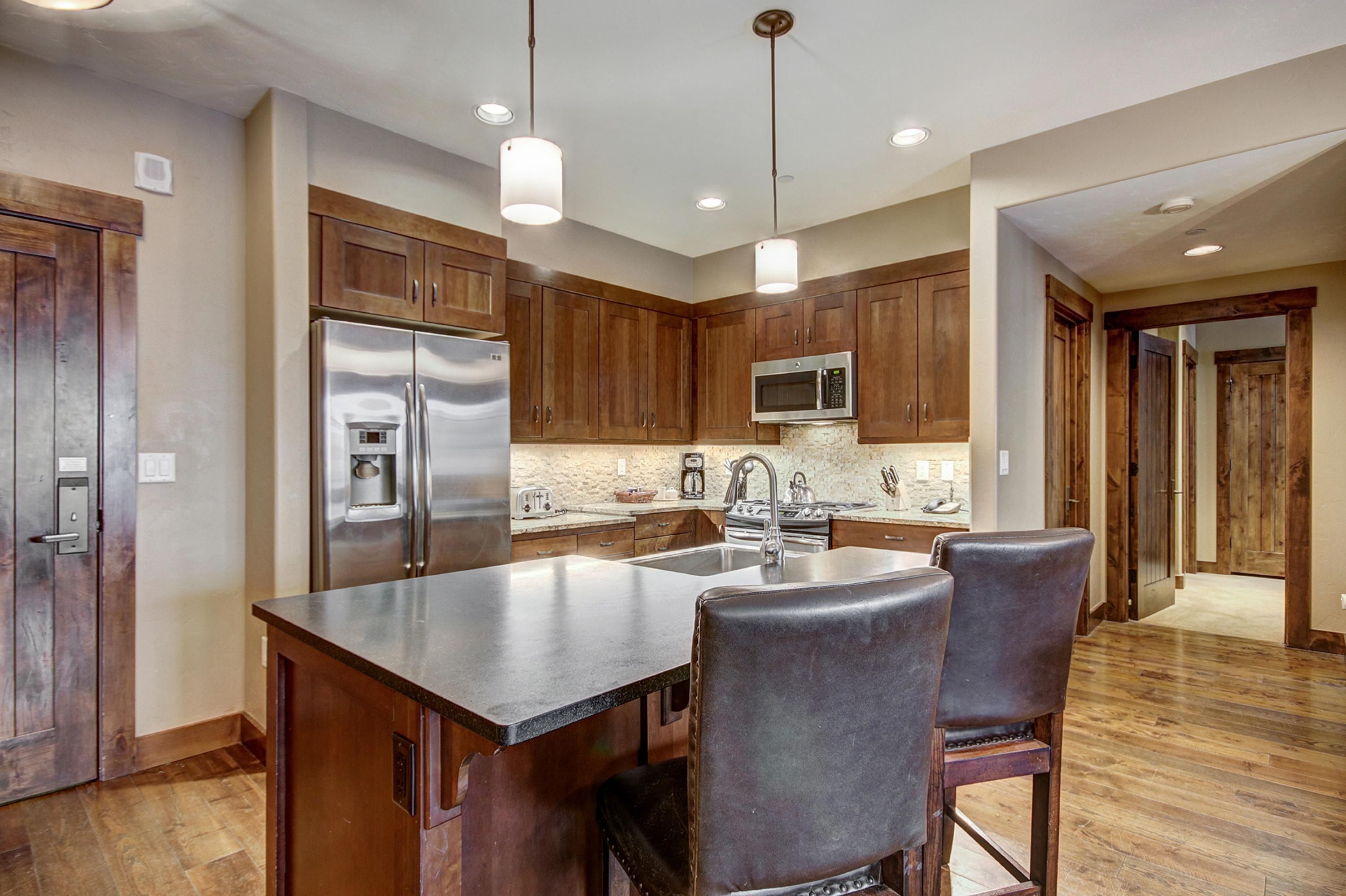 A kitchen with wooden cabinets, stainless steel appliances, a central island with bar stools, and pendant lighting.