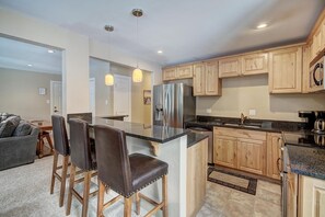 A modern kitchen with wooden cabinets, a stainless steel refrigerator, and a bar area with leather stools. - Tanenbaum BTR 201 in Columbine Rd (Columbine Rd)
