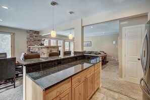 Eine Küche mit Granit-Arbeitsplatten, Holzschränken, Pendelleuchten und einem Kamin aus Naturstein.