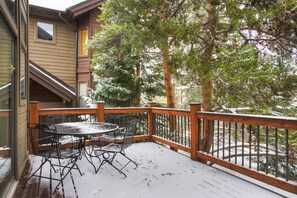 A covered outdoor deck with a table and chairs, surrounded by trees and a building. - Village Point 308 in Breckenridge (Breckenridge)