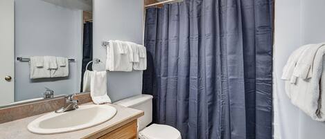 Une salle de bain équipée d’un lavabo, d’un miroir, de toilettes et d’un rideau de douche.