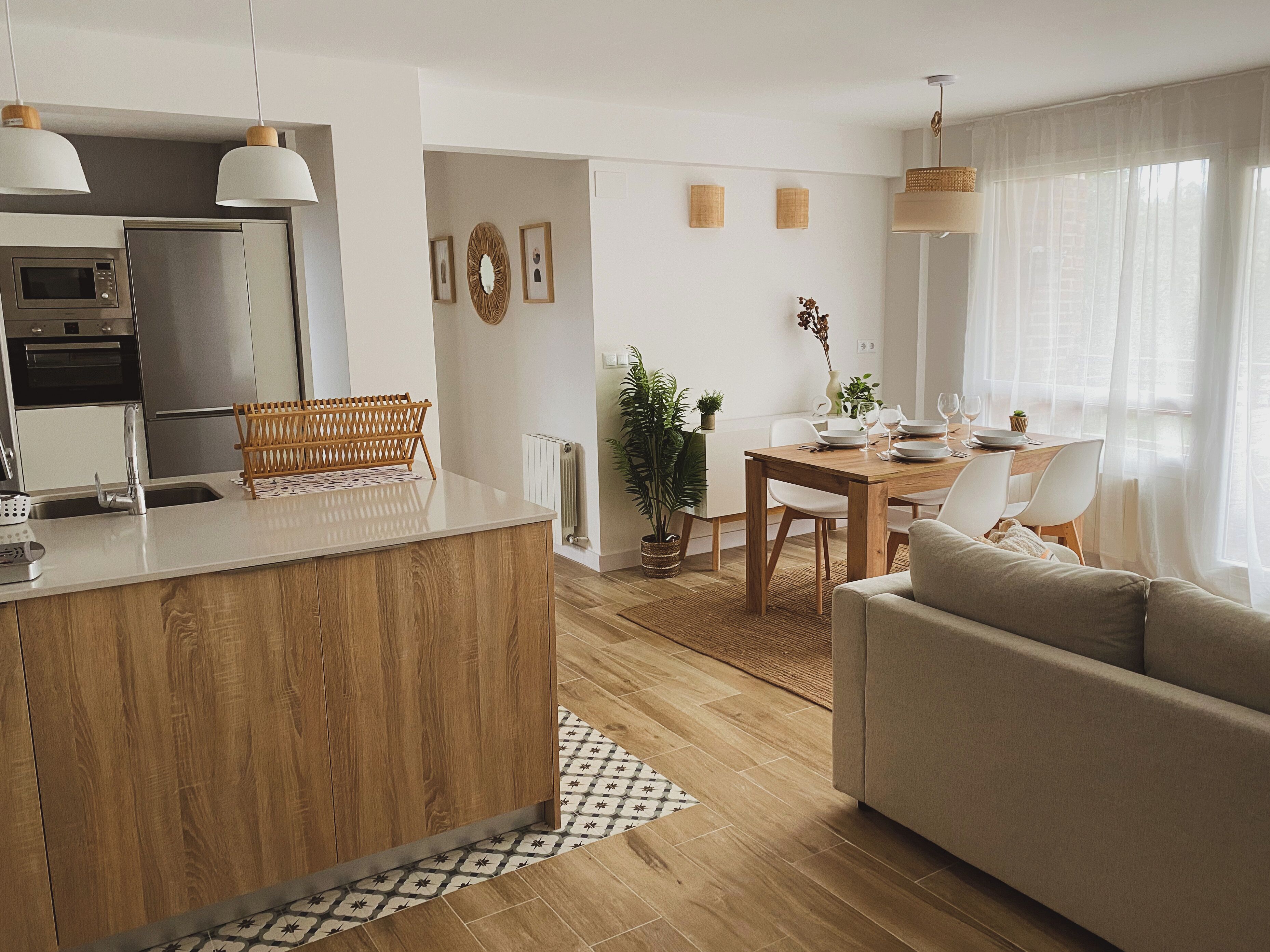 A modern kitchen with a central island, a dining area with a wooden table and chairs, and a living room with a sofa.