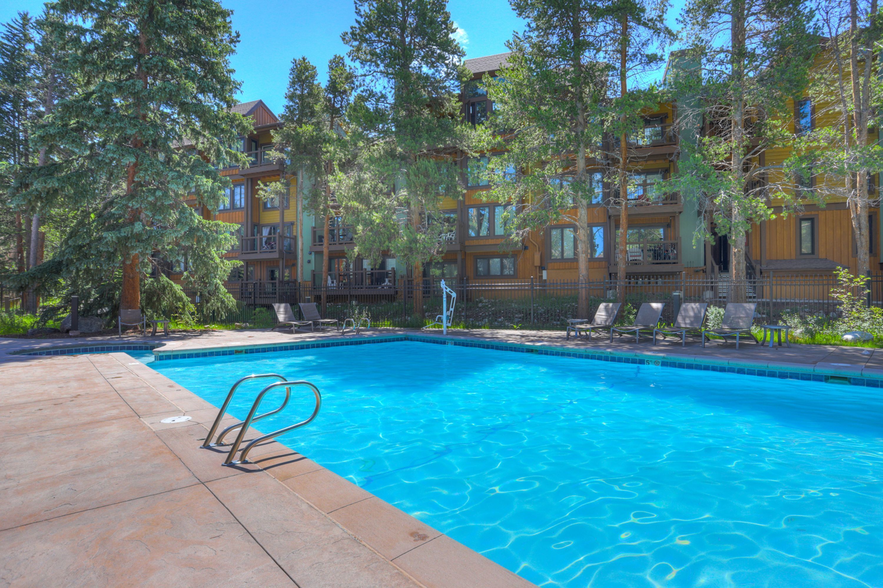 A swimming pool with a clear blue water surface, surrounded by a wooden deck and lounge chairs.