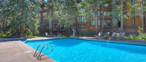 A swimming pool with a clear blue water surface, surrounded by a wooden deck and lounge chairs.
