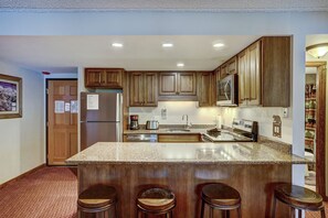 A kitchen with wooden cabinets, a granite countertop, a stainless steel refrigerator, and a built-in oven. - Trails End 201 in Breckenridge (Breckenridge)