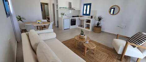 A modern living room with a sofa, a dining table, and a kitchen area with a refrigerator and stove.