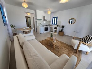 A modern living room with a sofa, a dining table, and a kitchen area with a refrigerator and stove. - White Wave Houses (Santorini)