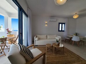 A modern living room with a sofa, coffee table, and dining area. - White Wave Houses (Santorini)