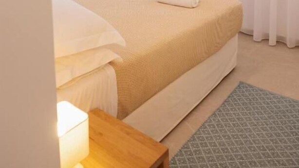 A bedroom with a bed, a flat-screen TV, an air conditioning unit, and a window with curtains. - White Wave Houses (Santorini)