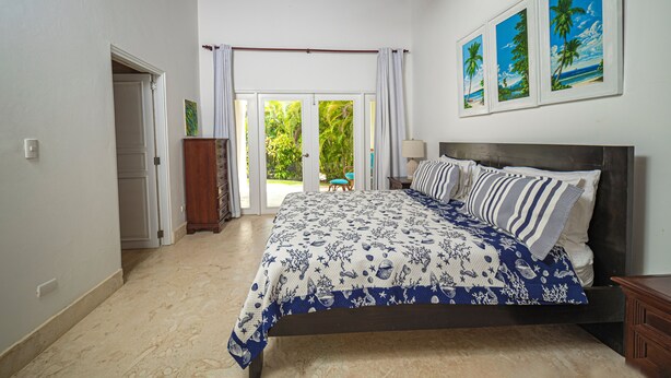 A bedroom with a bed, a ceiling fan, a door, and a window with curtains. - Villa Casamare Oceanfront Luxury in SeaHorseRanch (Sosúa)