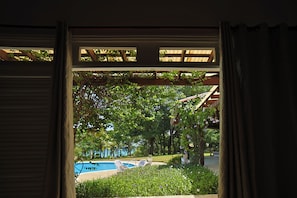 A view through a wooden-framed window with a view of a swimming pool, greenery, and a building structure. - Villa Casamare Oceanfront Luxury in SeaHorseRanch (Sosúa)