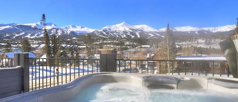 A hot tub with a view of snow-covered mountains and a town in the background.
