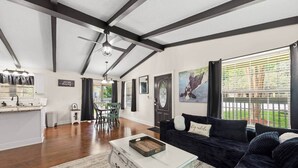 A spacious living area with a kitchen, dining table, and a black sofa with a cushion. - Sizzlin Farmhouse in Carencro (Lafayette Parish)