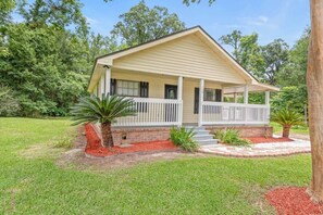 A single-story house with a front porch, a brick foundation, and a small front yard with red mulch and two palm trees. - Sizzlin Farmhouse in Carencro (Lafayette Parish)