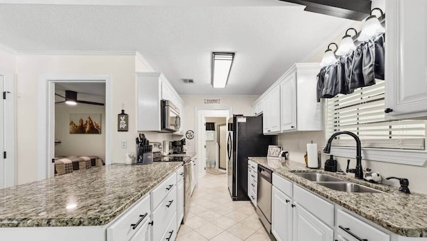 A kitchen with granite countertops, white cabinets, a black refrigerator, and a window with blinds. - Sizzlin Farmhouse in Carencro (Lafayette Parish)