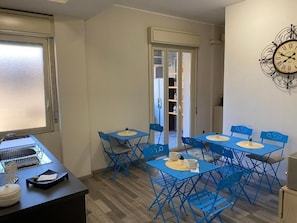Un coin repas avec des chaises et des tables bleues, un comptoir de cuisine avec un évier et une horloge murale.
