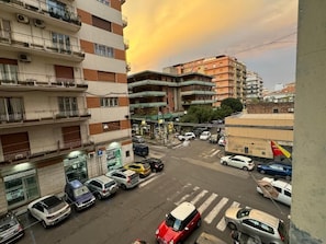 Un immeuble à plusieurs étages, doté de balcons, et un parking où sont garées différentes voitures.