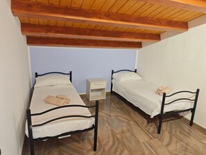 Ein Zimmer mit zwei Einzelbetten, einem kleinen Nachttisch und einer Holzbalkendecke.