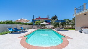 A swimming pool with blue lounge chairs, a red-roofed building in the background, and a clear blue sky. - Apartment 'Dea' with Shared Pool, Wi-Fi, and Air Conditioning (Arenella)