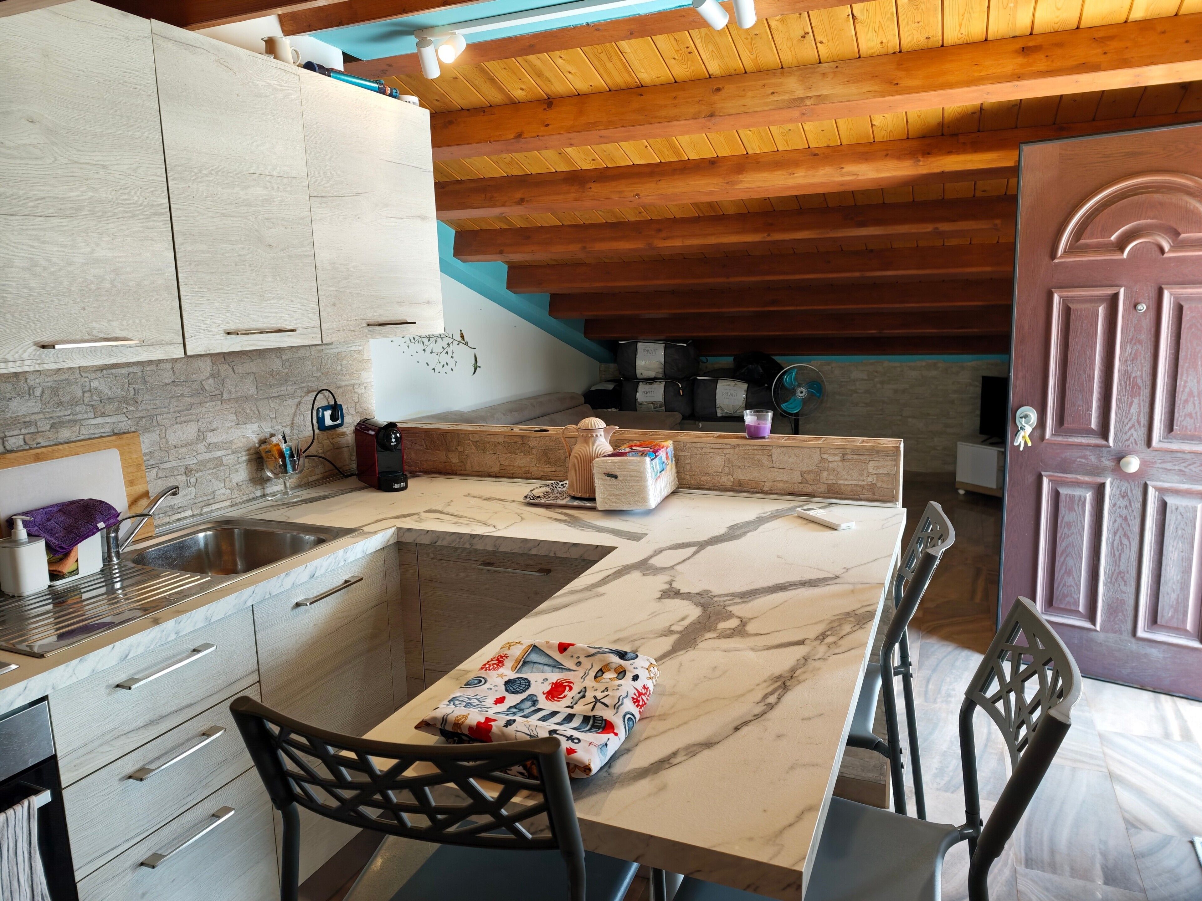 A kitchen with a marble countertop, wooden cabinets, a dining area with a table and chairs, and a wooden ceiling.