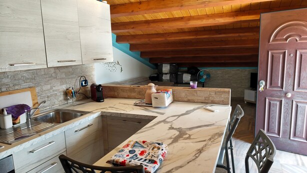A kitchen with a marble countertop, wooden cabinets, a dining area with a table and chairs, and a wooden ceiling. - Apartment 'Dea' with Shared Pool, Wi-Fi, and Air Conditioning (Arenella)