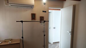 A room with a standing fan, a door, a wall-mounted air conditioner, and a wooden desk with a framed picture and a roll of paper. - Apartment 'Dea' with Shared Pool, Wi-Fi, and Air Conditioning (Arenella)