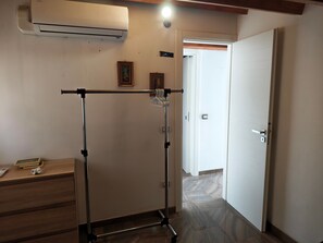 Ein Zimmer mit Standventilator, einer Tür, einer Wand-Klimaanlage und einem Holztisch mit gerahmtem Bild und einer Papierrolle.