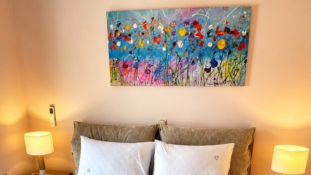 Ein ordentlich bezogenes Bett mit weißen Leinentüchern, zwei Nachttischlampen, ein Gemälde an der Wand und ein hölzernes Kopfteil.