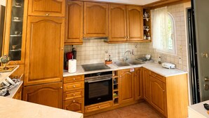 Eine Küche mit Holzschränken, einem Einbauofen, einer Spüle und einem Fenster mit Vorhängen.