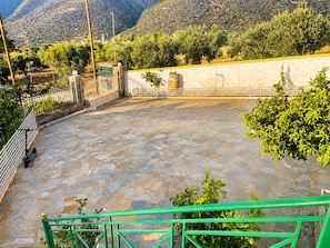 A courtyard with stone flooring, a green metal railing, and a view of a mountainous landscape. - Suite Sunset, Overlooking the Sea in Ag. Vasilios (Agios Vasilios)