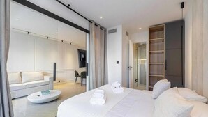 Et moderne hotelværelse med en stor seng, et siddeområde med sofa og lænestol, et fladskærms-tv og et walk-in closet.