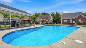 En klar, blå swimmingpool med en dybdemarkering på 1,5 meter, omgivet af et indhegnet område med liggestole og et overdækket siddeområde.