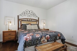 A bedroom with a wooden headboard, a floral bedspread, two bedside tables with lamps, and a wooden bench. - Entire Home Close to Pigeon Forge (Pigeon Forge)