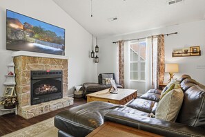 A living room with a stone fireplace, leather sofa, and a television mounted on the wall. - Entire Home Close to Pigeon Forge (Pigeon Forge)