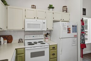 A kitchen with white cabinets, a microwave, stove, refrigerator, and a red apron hanging on the door. - Entire Home Close to Pigeon Forge (Pigeon Forge)