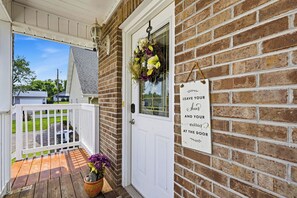 Eine Veranda mit einer weißen Tür, einer Ziegelwand und einem Schild, auf dem steht: 'LEAVE YOUR shoes AND YOUR worries AT THE DOOR'.