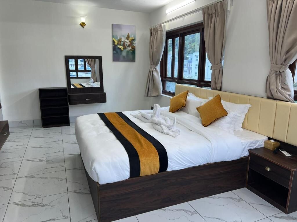 Habitación de hotel con cama, mesita de noche, espejo y ventana con cortinas.