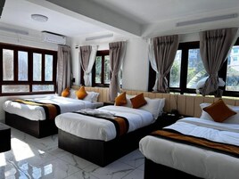 Quarto de hotel com três camas, janelas amplas e ar condicionado.