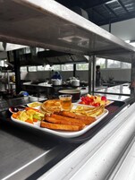 Uma bandeja com comida, incluindo panquecas, omeletes e vegetais, acompanhada de uma bebida e uma tigela de frutas.