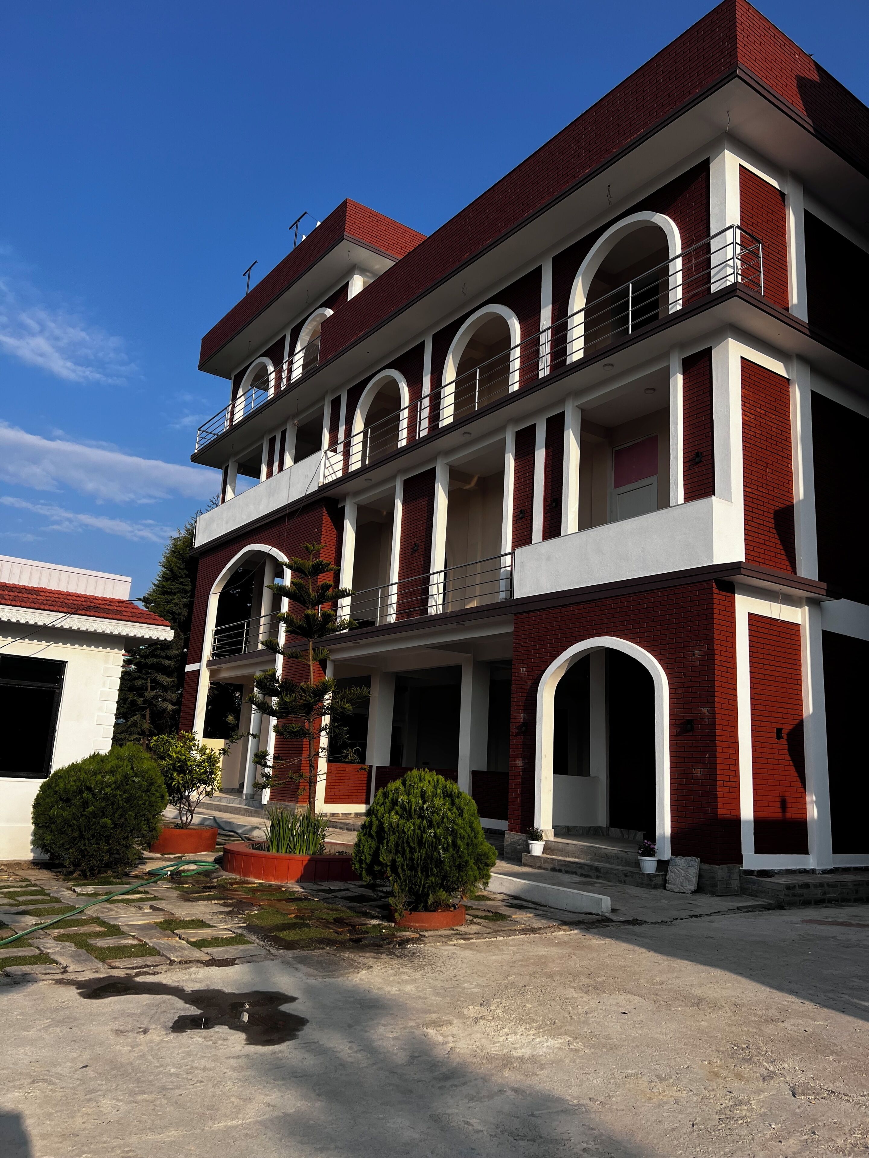Um edifício de vários andares com fachada vermelha e branca, várias varandas e um pátio com plantas em vasos.