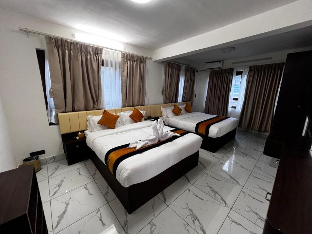 Habitación de hotel con dos camas, una mesita de noche, cabecera de madera y suelo de mármol.