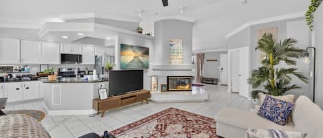 Una sala de estar moderna con chimenea, televisor y zona de cocina.
