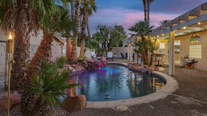 A swimming pool surrounded by palm trees and a stone wall, with a building in the background. - Unwind in Henderson | Pool, Spa & Spacious Retreat (Henderson)