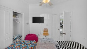 A bedroom with a ceiling fan, a bed with patterned bedding, a pink bean bag, a checkered ottoman, and a television on the wall. - Unwind in Henderson | Pool, Spa & Spacious Retreat (Henderson)