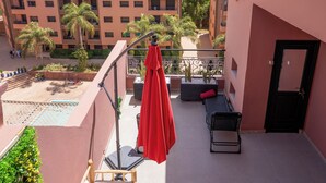 Ein Balkon mit einem roten Sonnenschirm, einem Pool und Blick auf ein Wohngebäude.